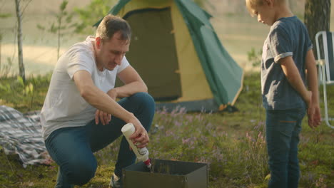 father-and-son-are-inflaming-coals-in-chargrill-picnic-and-rest-at-nature-family-trip-in-forest-and-stay-in-tent-camp